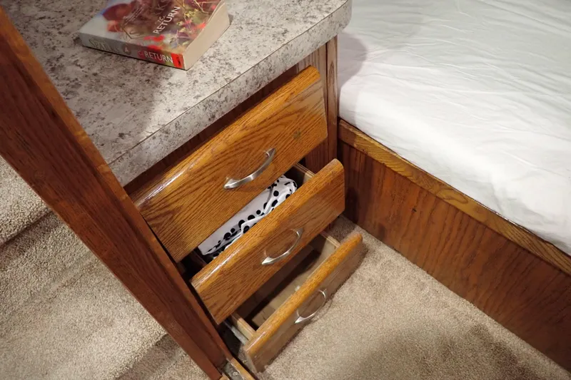 Slide: The Image of 1988 Mainship interior with wooden drawers, countertop, and book, next to a bed. - 78