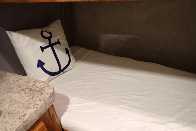 Slide: The Image of 1988 Mainship cabin bed with anchor-themed pillow and white bedding. - 80