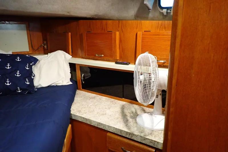 Slide: The Image of 1988 Mainship cabin interior with bed, anchor-themed pillows, fan, and wooden cabinets. - 81
