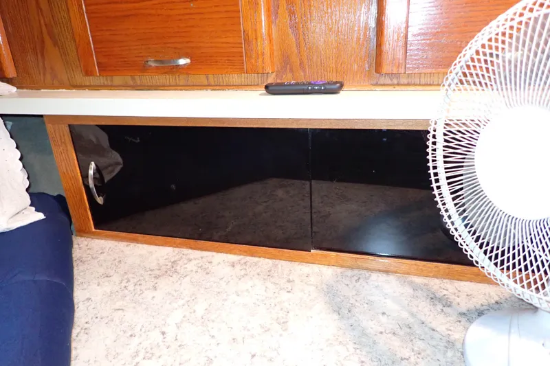 Slide: The Image of 1988 Mainship interior with wooden cabinets, countertop, fan, and remote control. - 85