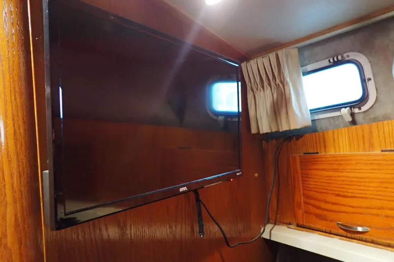 Slide: The Image of 1988 Mainship interior with mounted TV, wooden paneling, and small window with curtain. - 92