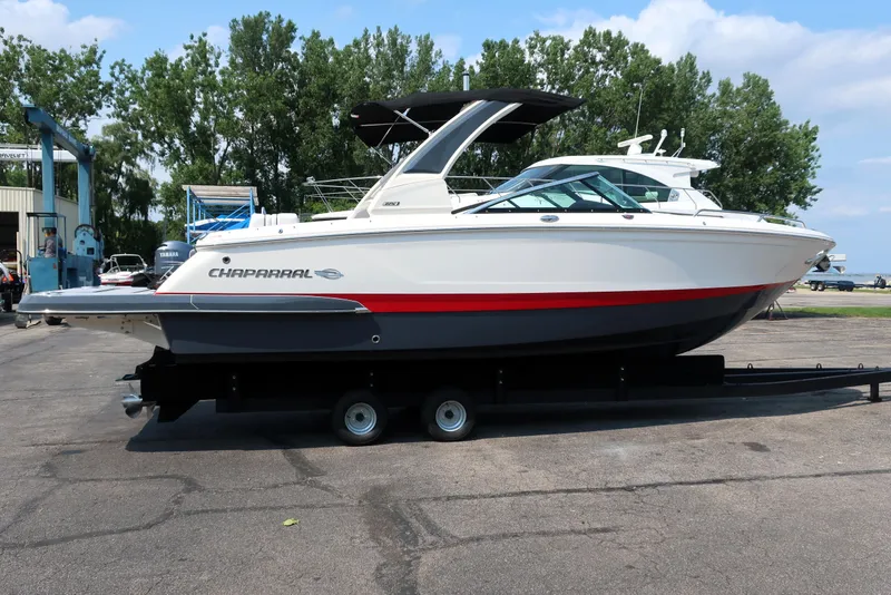Slide: The Image of 2021 Chaparral 267 SSX boat on trailer, parked outdoors with trees in background. - 2