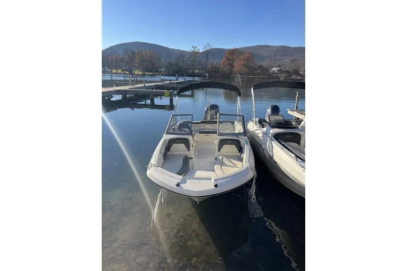 The Image of 2016 Stingray 191 DC boat docked on a serene lake with scenic mountain backdrop. - 1