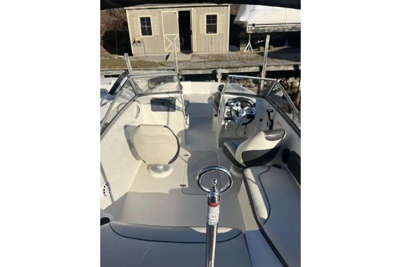 Slide: The Image of 2016 Stingray 191 DC boat interior with steering wheel and seating, docked near a shed. - 4