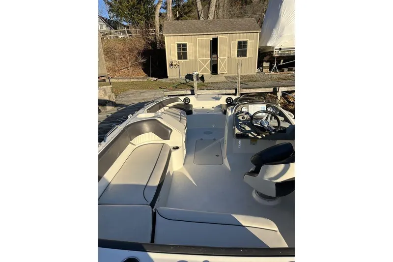 Slide: The Image of 2016 Stingray 192 SC boat interior with seating and steering wheel, docked near a wooden shed. - 12
