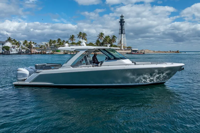 Slide: The Image of 2019 Tiara Sport 38 LS boat cruising near a lighthouse, under a partly cloudy sky. - 2
