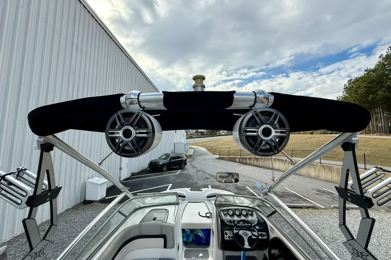 Slide: The Image of 2010 Yamaha Boats 212X with wakeboard tower and speakers, parked near a building under cloudy skies. - 5