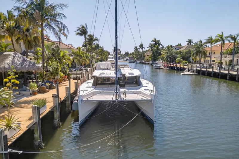 Slide: The Image of 2021 Leopard 50 catamaran docked in a tropical canal with palm trees. - 2