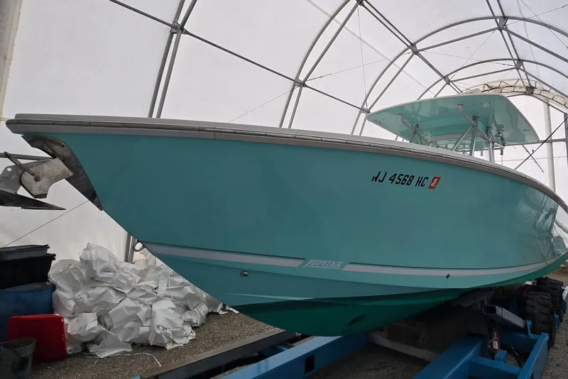 The Image of 2010 Jupiter 34 FS boat in storage, turquoise hull, under a protective canopy. - 0