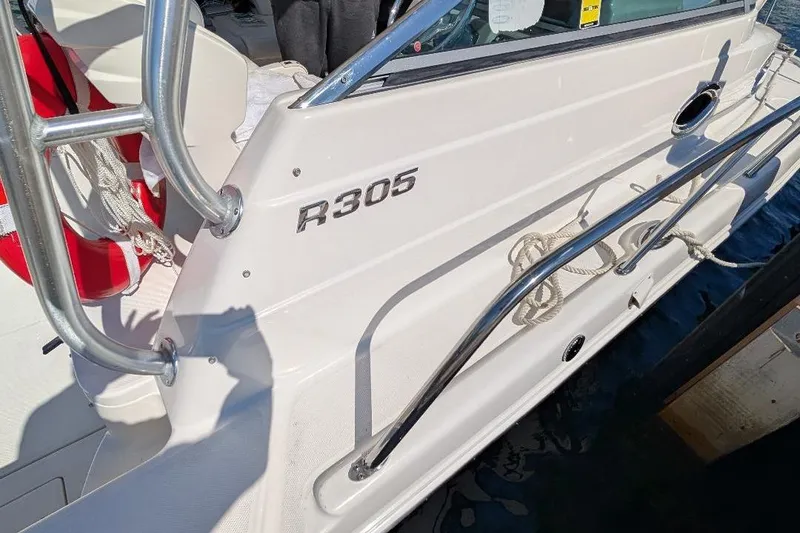 Slide: The Image of 2014 Robalo R305 Walkaround boat docked, featuring sleek design and safety equipment. - 15