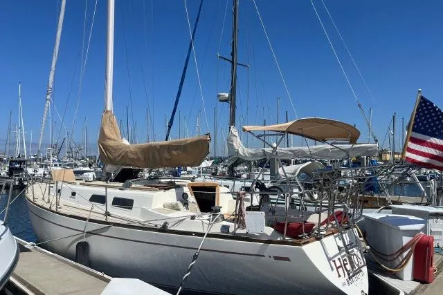 The Image of 1980 CAL 39 sailboat docked at marina with American flag, clear blue sky. - 1
