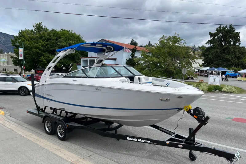 The Image of 2024 Regal LS4 Surf boat on trailer, parked on street with trees and buildings in background. - 1