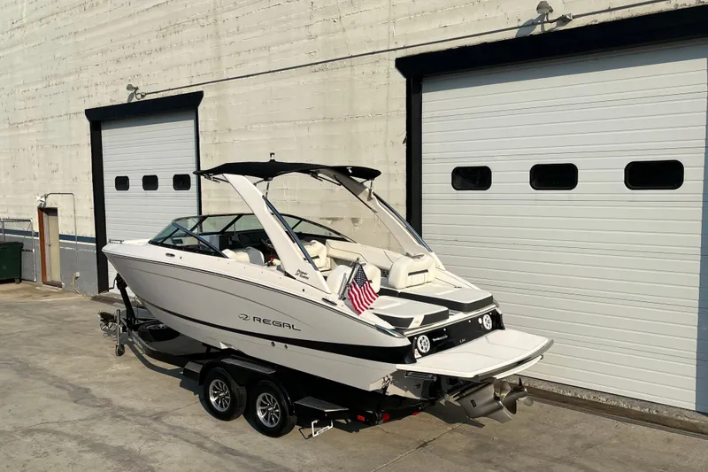 Slide: The Image of 2025 Regal LS4 boat on trailer, parked outside large garage doors. - 2