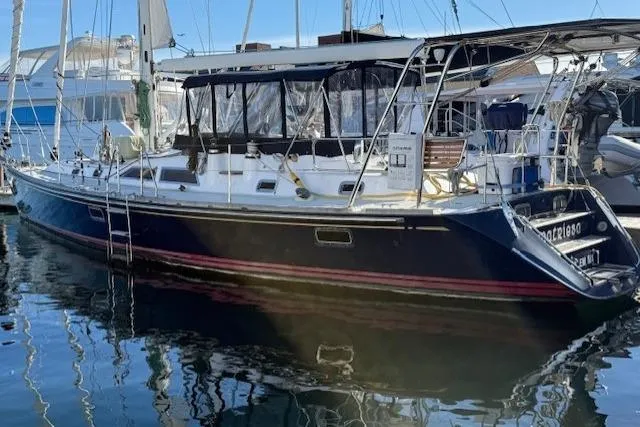 Slide: The Image of 2002 Hylas 46 sailboat docked in marina, featuring sleek design and spacious deck. - 2