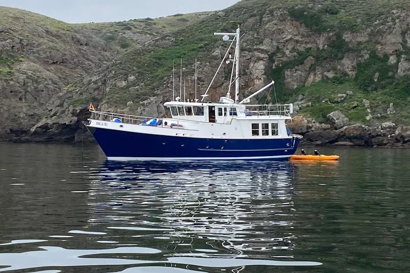 The Image of 1989 Nordhavn 46 yacht anchored near rocky coastline with kayak nearby. - 1