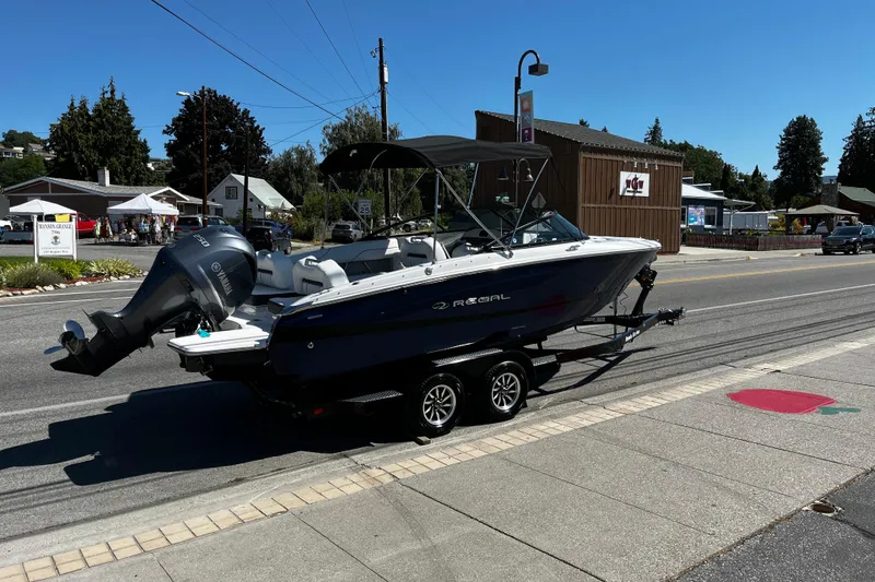 Slide: The Image of 2026 Regal LX2 boat on trailer, parked on street under clear blue sky. - 2