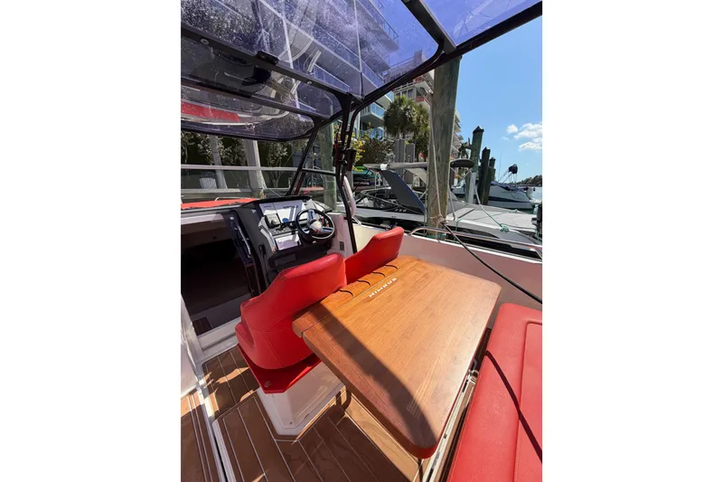 Slide: The Image of 2021 Nimbus T8 boat interior with red seating and wooden table, docked at marina. - 52