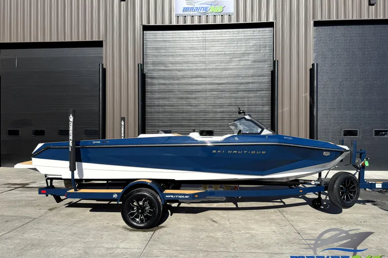 The Image of 2026 Nautique Ski Nautique boat on trailer, parked outside a warehouse. - 0