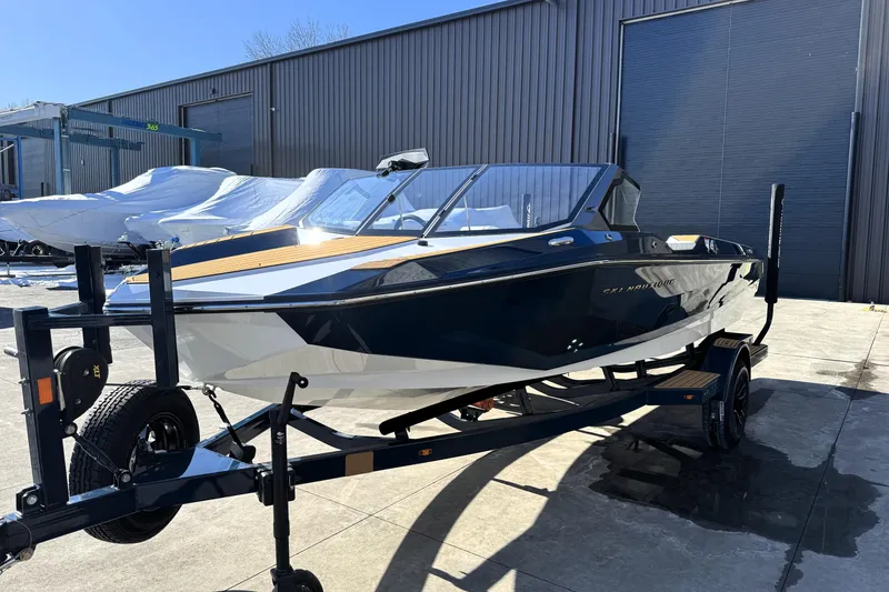 Slide: The Image of 2026 Nautique Ski Nautique boat on trailer, parked outside a warehouse. - 2