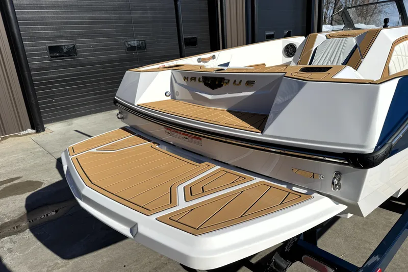 Slide: The Image of 2026 Nautique Ski Nautique boat with teak deck, parked outside a garage. - 28