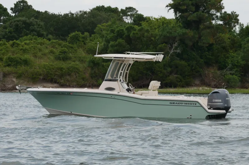 Slide: The Image of 2021 Grady-White Fisherman 236 boat on water, featuring Yamaha engine, lush green shoreline background. - 2