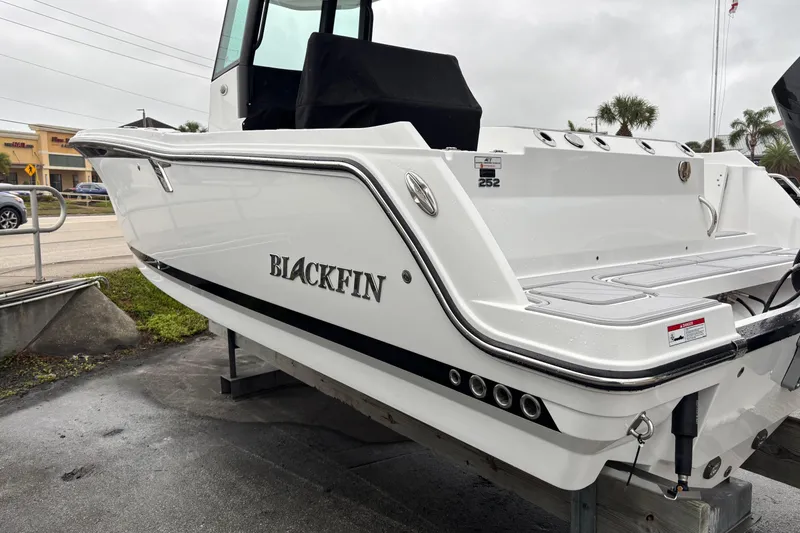 Slide: The Image of 2025 Blackfin 252 CC boat, sleek white design, parked outdoors on a cloudy day. - 2