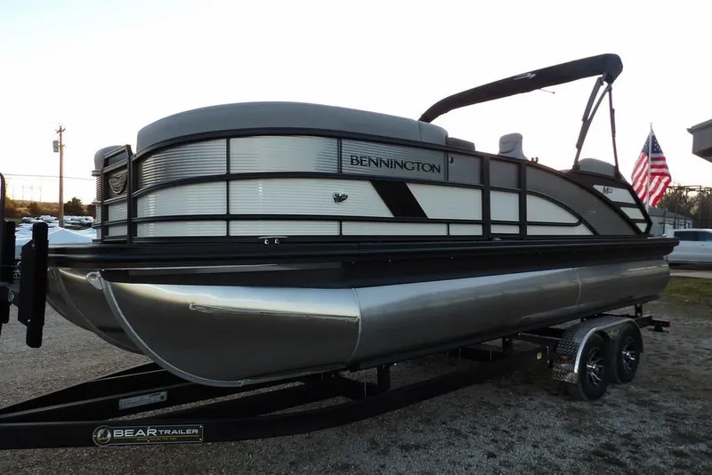 Slide: The Image of 2026 Bennington M Swingback 22 MSB pontoon boat on trailer, American flag in background. - 2