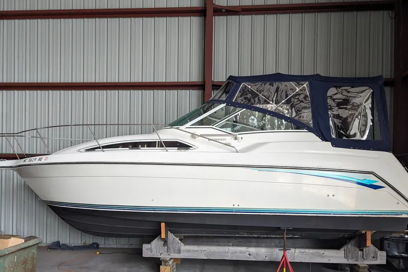The Image of 1995 Carver 250 Express boat in storage, featuring a sleek white design and blue accents. - 1