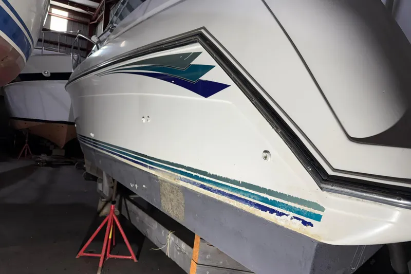 Slide: The Image of 1995 Carver 250 Express boat in storage, showing side view with colorful stripes. - 27