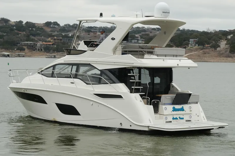 Slide: The Image of 2018 Sea Ray Fly 460 yacht cruising on a lake with scenic shoreline views. - 21