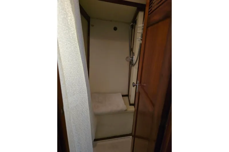 Slide: The Image of Compact shower area in a 1982 Irwin 52 sailboat, featuring wooden accents and a handheld showerhead. - 25