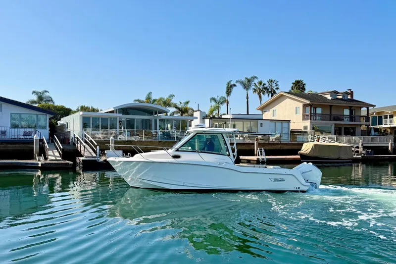 Slide: The Image of 2025 Boston Whaler 285 Conquest cruising near waterfront homes under clear blue skies. - 11