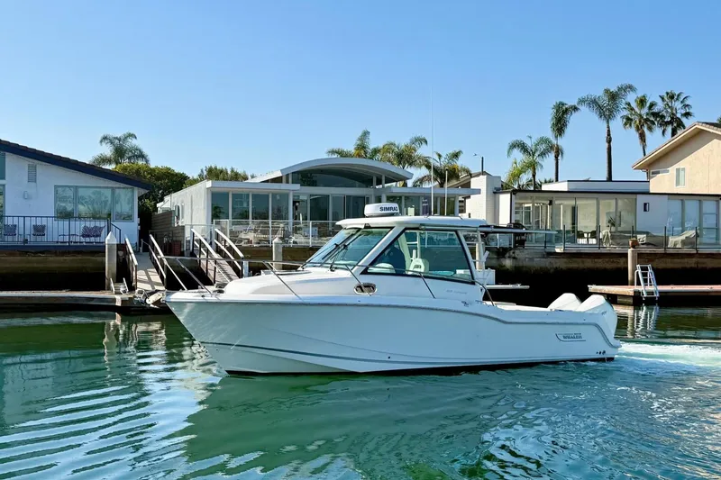 Slide: The Image of 2025 Boston Whaler 285 Conquest boat docked near waterfront homes with palm trees. - 7