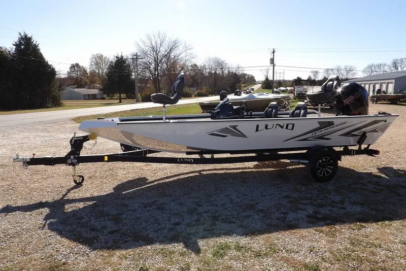 Slide: The Image of 2026 Lund 1875 Renegade fishing boat on trailer, parked outdoors in a sunny setting. - 4