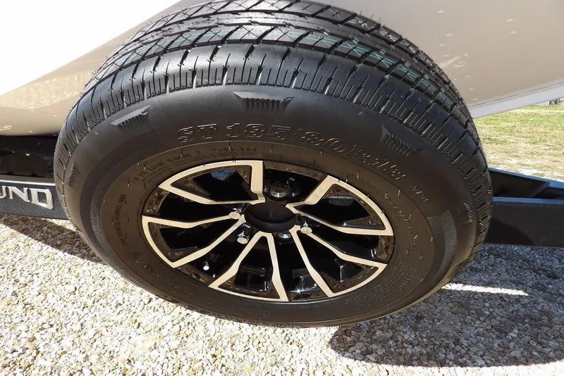 Slide: The Image of 2026 Lund 1875 Renegade trailer tire with black and silver alloy wheel on gravel. - 42