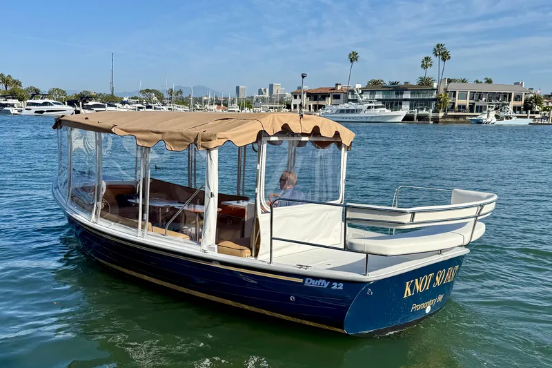 Slide: The Image of 2022 Duffy Suncruiser 22 boat on water, featuring a tan canopy and clear side panels. - 2