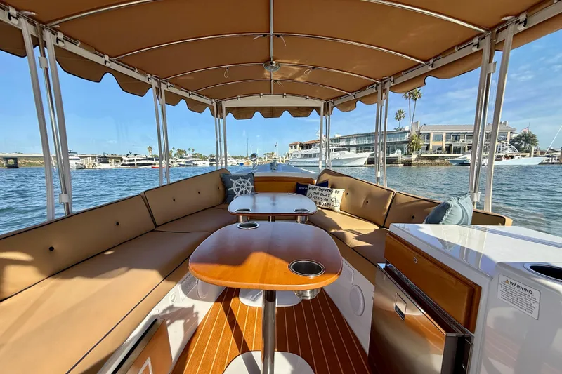 Slide: The Image of 2022 Duffy Suncruiser 22 boat interior with tan seating and wooden tables on the water. - 3