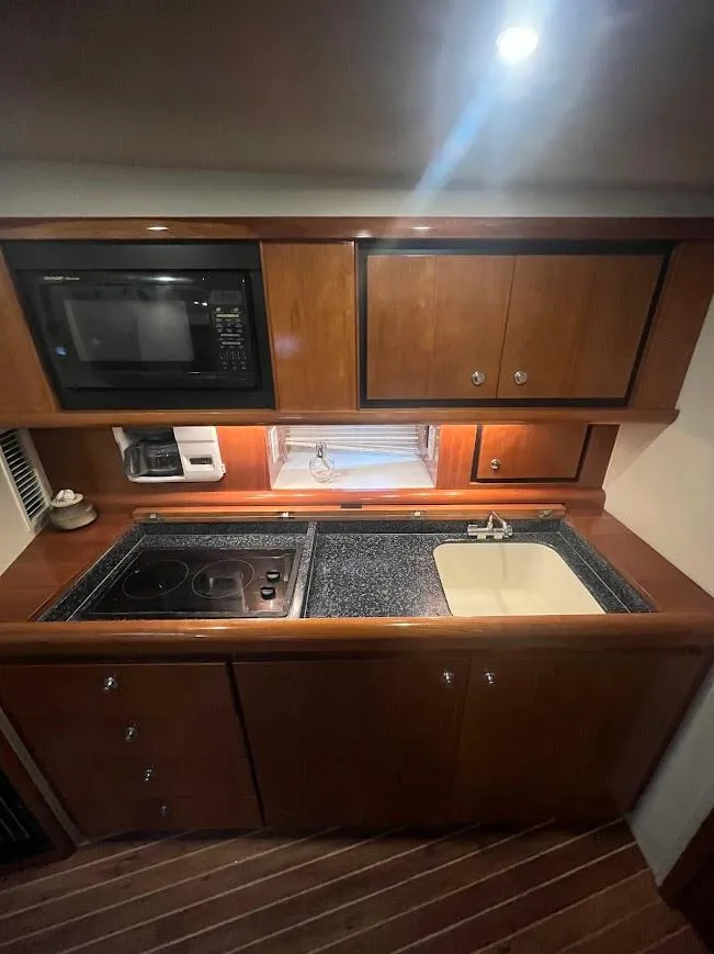 Slide: The Image of 2000 Carver 440 Hardtop Express kitchen with microwave, stove, sink, and wooden cabinets. - 17