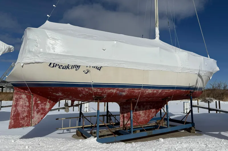 The Image of 1979 O'Day 37 sailboat, named "Breaking Wind," covered and stored on a snowy dock. - 1