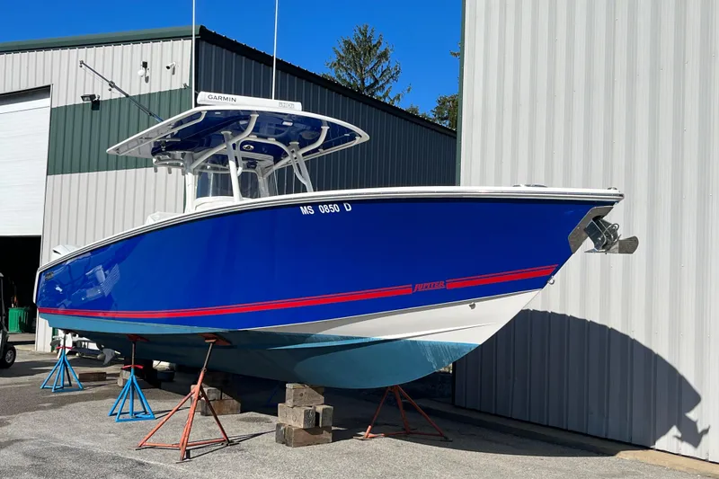 The Image of 2020 Jupiter 34 Center Console boat in vibrant blue, elevated on stands outside a warehouse. - 1