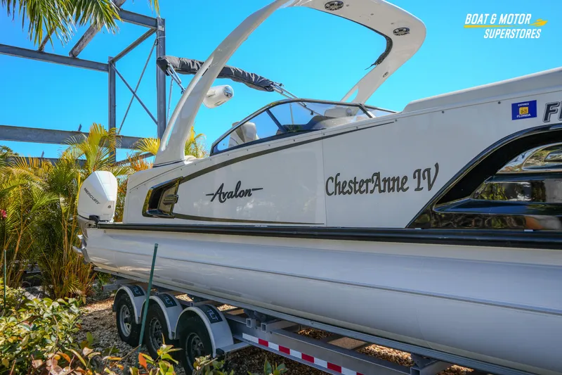 Slide: The Image of 2024 Avalon Twin Quad Lounger Windshield boat on trailer, surrounded by tropical plants. - 14