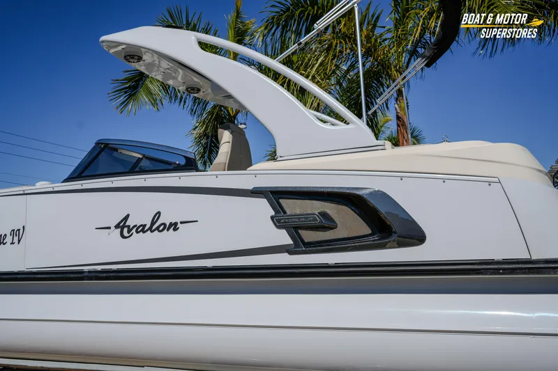Slide: The Image of 2024 Avalon Twin Quad Lounger Windshield boat with sleek design and palm trees background. - 5
