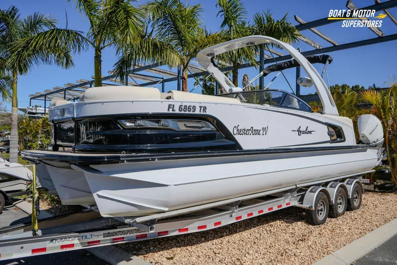 Slide: The Image of 2024 Avalon Twin Quad Lounger Windshield boat on trailer, surrounded by palm trees. - 7