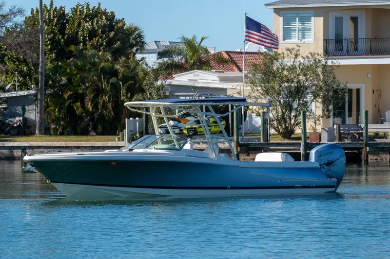 The Image of 2018 Chris-Craft Calypso 26 boat docked near waterfront home with American flag. - 0