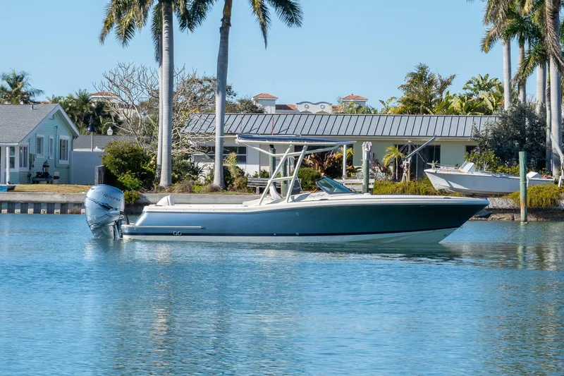 Slide: The Image of 2018 Chris-Craft Calypso 26 boat on calm water, surrounded by palm trees and houses. - 2