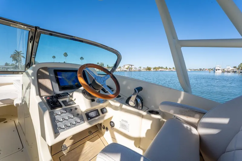 Slide: The Image of 2018 Chris-Craft Calypso 26 boat cockpit with steering wheel and control panel, overlooking serene waters. - 27