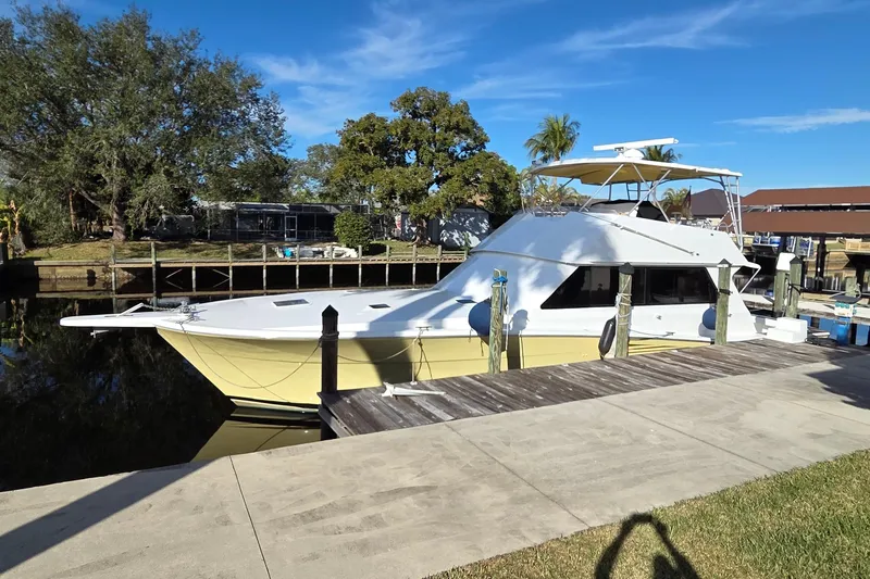 The Image of 1990 Viking 53 Convertible yacht docked by a wooden pier, surrounded by trees. - 0