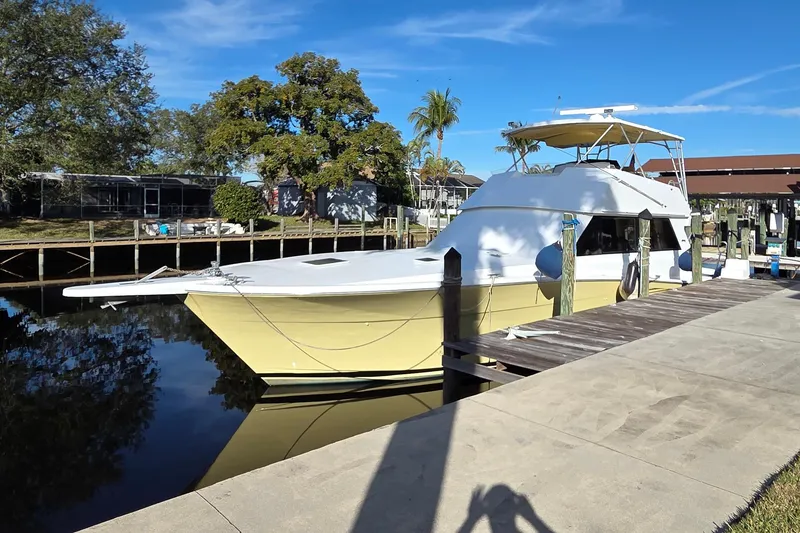 Slide: The Image of 1990 Viking 53 Convertible yacht docked by a wooden pier, surrounded by trees and clear blue sky. - 96