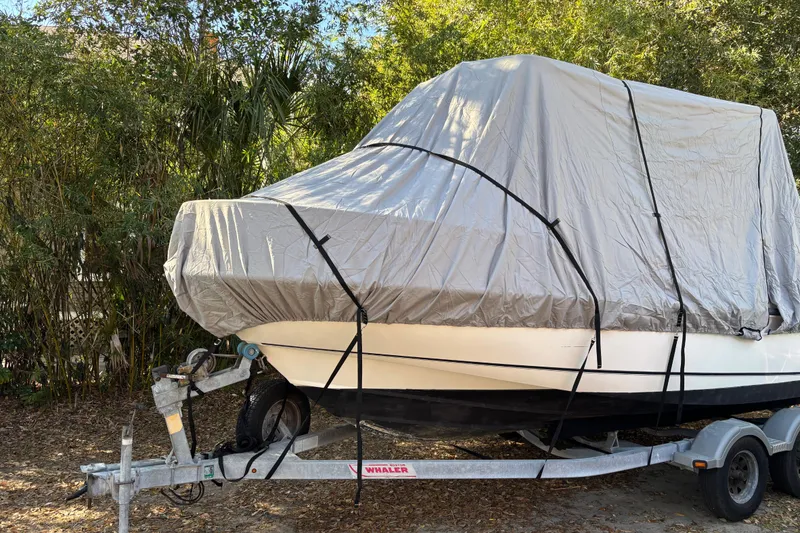 Slide: The Image of 2015 Boston Whaler 190 Outrage boat covered on trailer, surrounded by greenery. - 11