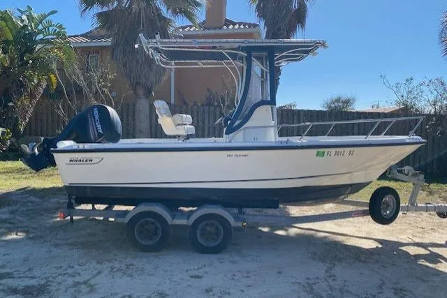 Slide: The Image of 2015 Boston Whaler 190 Outrage boat on trailer, parked outdoors. - 2